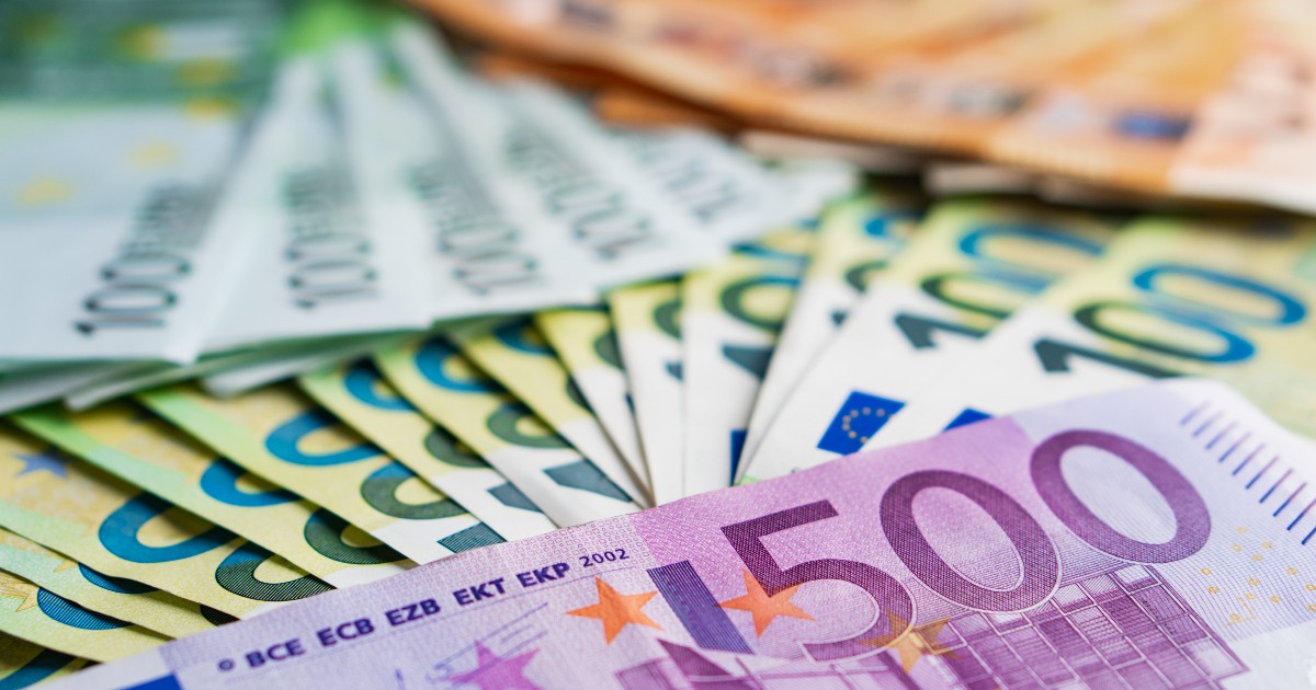 Imaginea este un prim-plan al unei colecții de bancnote euro de valori diferite, cu o bancnotă de 500 de euro de culoare violet în prim-plan, acoperind parțial celelalte bancnote. În fundal, se văd bancnote de 100 de euro de culoare verde și portocalie, dispuse în evantai, sugerând o sumă mare de bani.