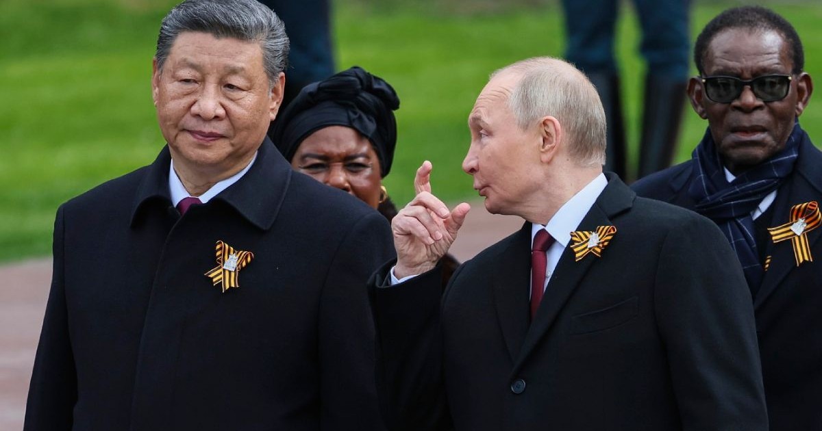În imagine președintele rus Vladimir Putin s-a întâlnit cu președintele chinez Xi Jinping în Rusia, de Ziua Victoriei, îmbrăcați in negru , in aer liber, Putin cu fata intoarsa săre Xi , cu mana dreaptă ridicata, arătând ceva cu degetul arătător, în spate alte doua persoane de culoare