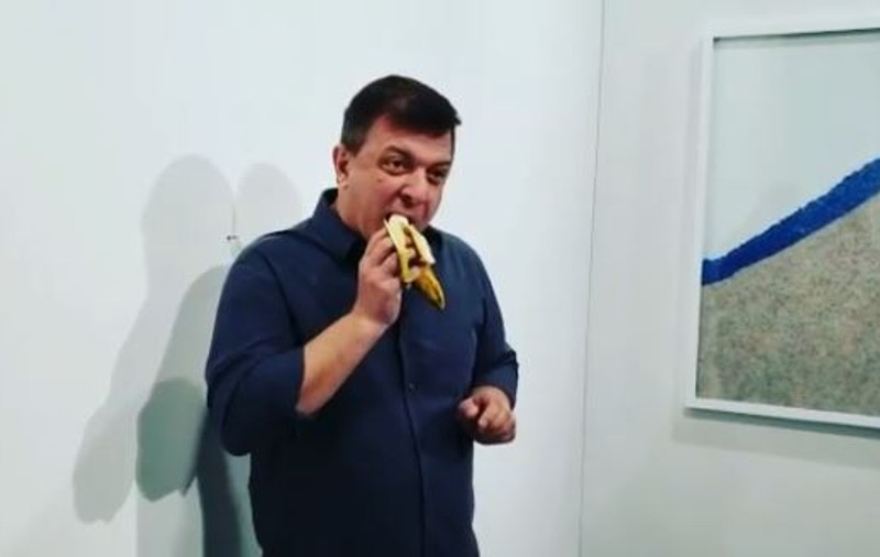 VIDEO | Banana lipită cu bandă adezivă pe un perete și vândută cu 120.000 de dolari, mâncată de un "Artist Flămând": "Ador această instalaţie. E foarte delicioasă"