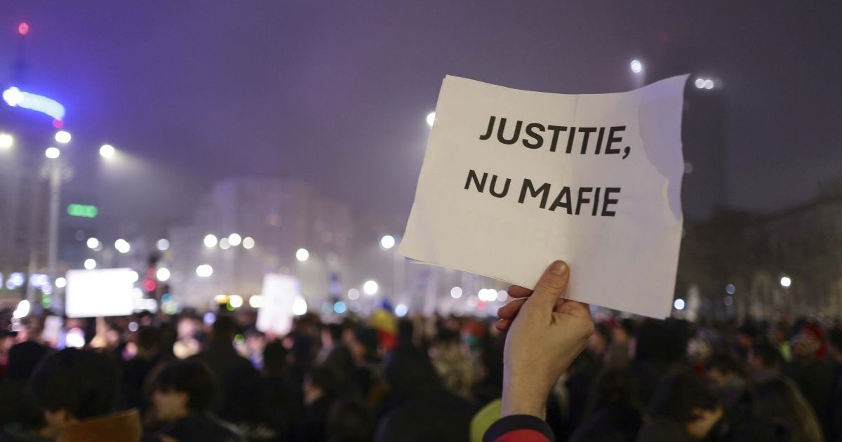 Un bărbat ține în mână o foaie pe care scrie „Justiție, nu mafie” la protestul din Piața Victoriei din 11 decembrie 2025