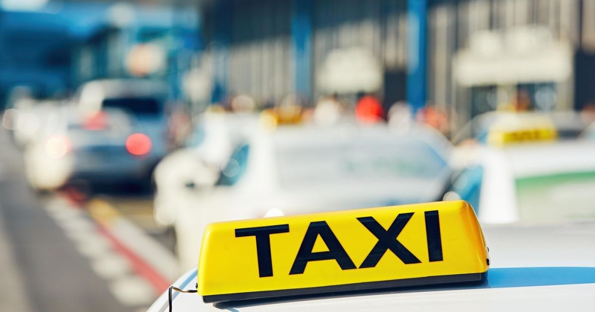 O mașină de taxi pe stradă, lângă alte autoturisme, în fața unui aeroport