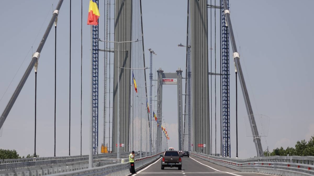 podul suspendat peste Dunăre de la Brăila, cu mașini care circula pe drum și stegulețe tricolore arborate de-a lungul cablurilor de susținere, fără trafic intens