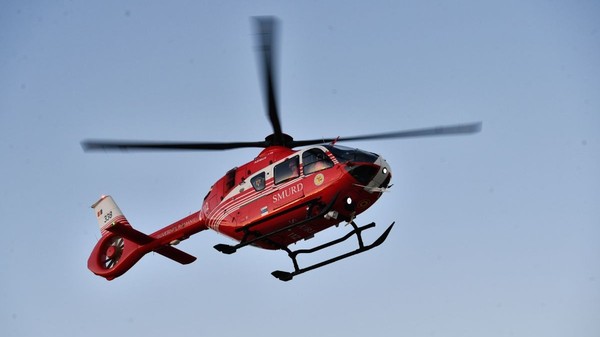 Elicopter SMURD, de culoare roșie, aflat în zbor, cu cerul albastru pe fundal