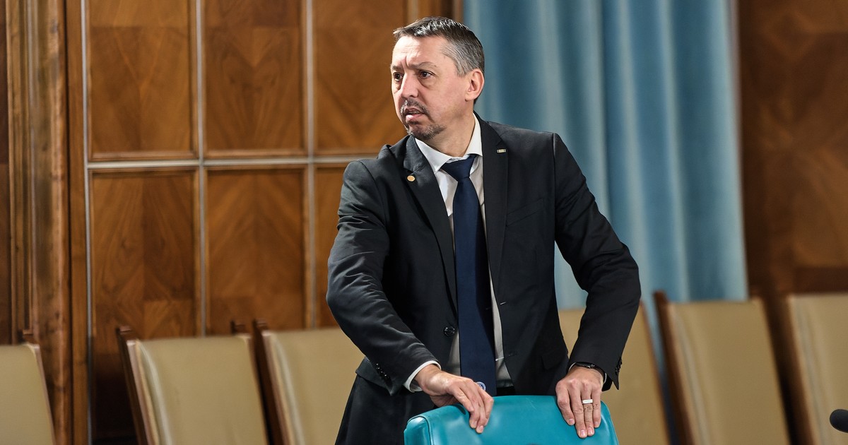 Ministrul Educației, Daniel David, stă în picioare, în spatele unui scaun gol, intr-o sală de conferințe