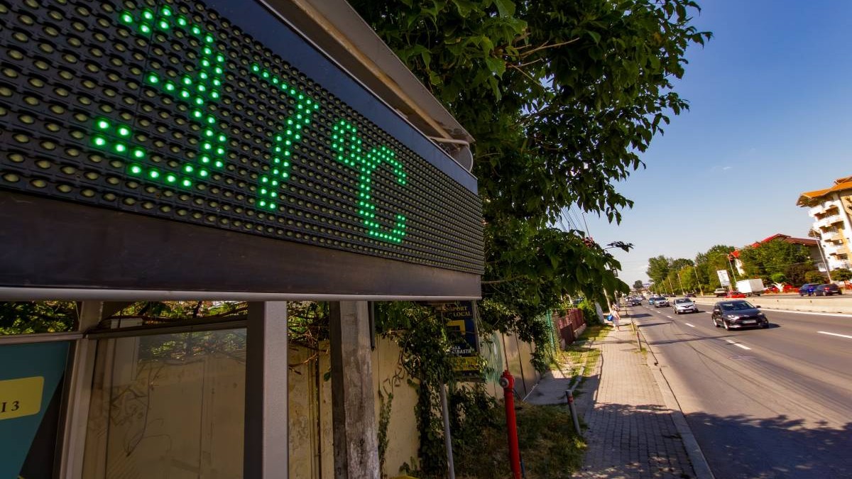 Un termometru stradal care indică temperatura de 37 de grade Celsius pe un bulevard însorit