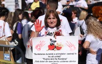 O femeie aflată în mijlocul protestatarilor își ridică palma acoperită cu vopsea roșie și ține o pancartă cu imaginile unui cățel și ale unei pisici alături de mesaje de protecție a animalelor.