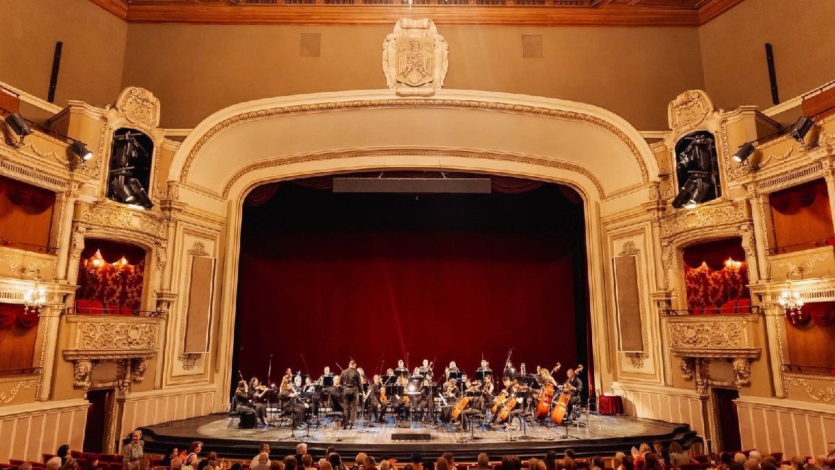 Scena Operei Naționale București, plină de muzicieni, în spate se vede cortina roșie