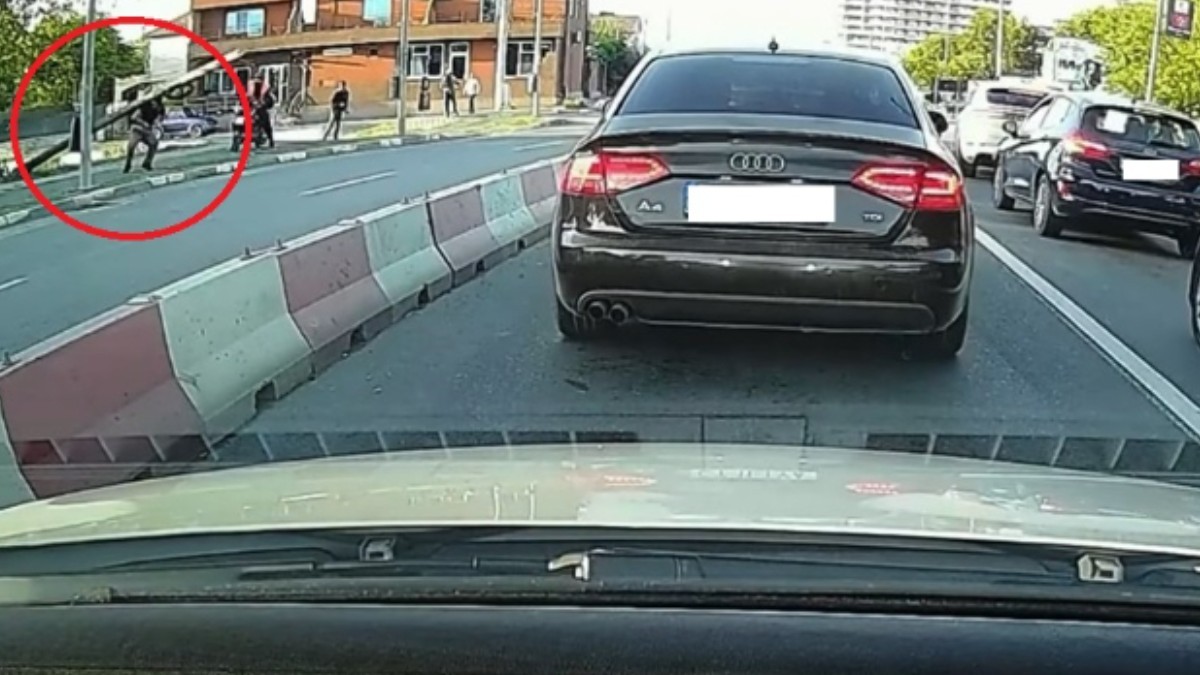 Un bărbat care a fost lovit în cap de un stâlp, pe trotuar. Pe șosea se observă mai multe mașini