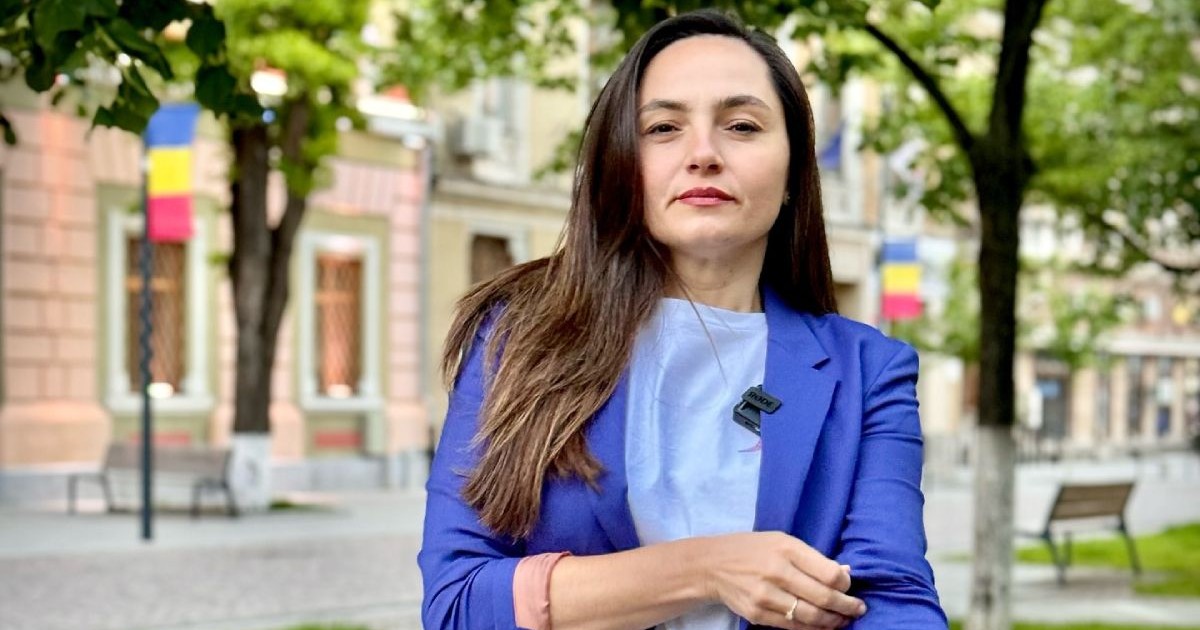 Anamaria Gavrilă, președinta POT, în fața unei clădiri de culoare maro, cu copaci pe fundal, îmbrăcată cu o bluză bleumarin și un sacou albastru