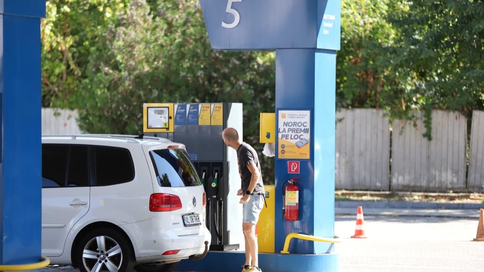 Un bărbat care se uită la ecranul unei pompe dintr-o stație de carburanți, lângă un autoturism alb Volkswagen parcat pentru alimentare.