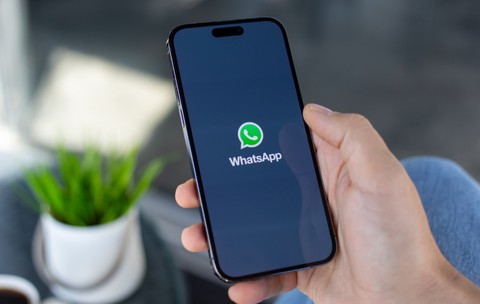 O persoană care ține un telefon în mână și deschide aplicația WhatsApp