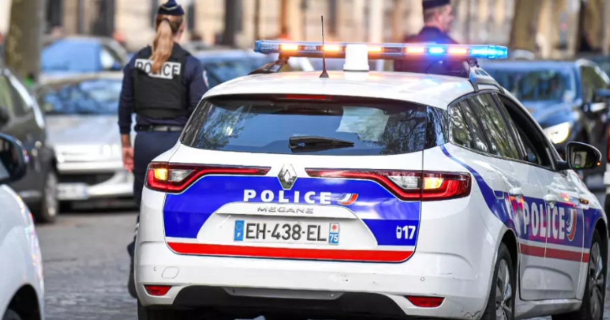 O mașină de poliție parcată pe stradă. Lângă ea se află doi polițiști.