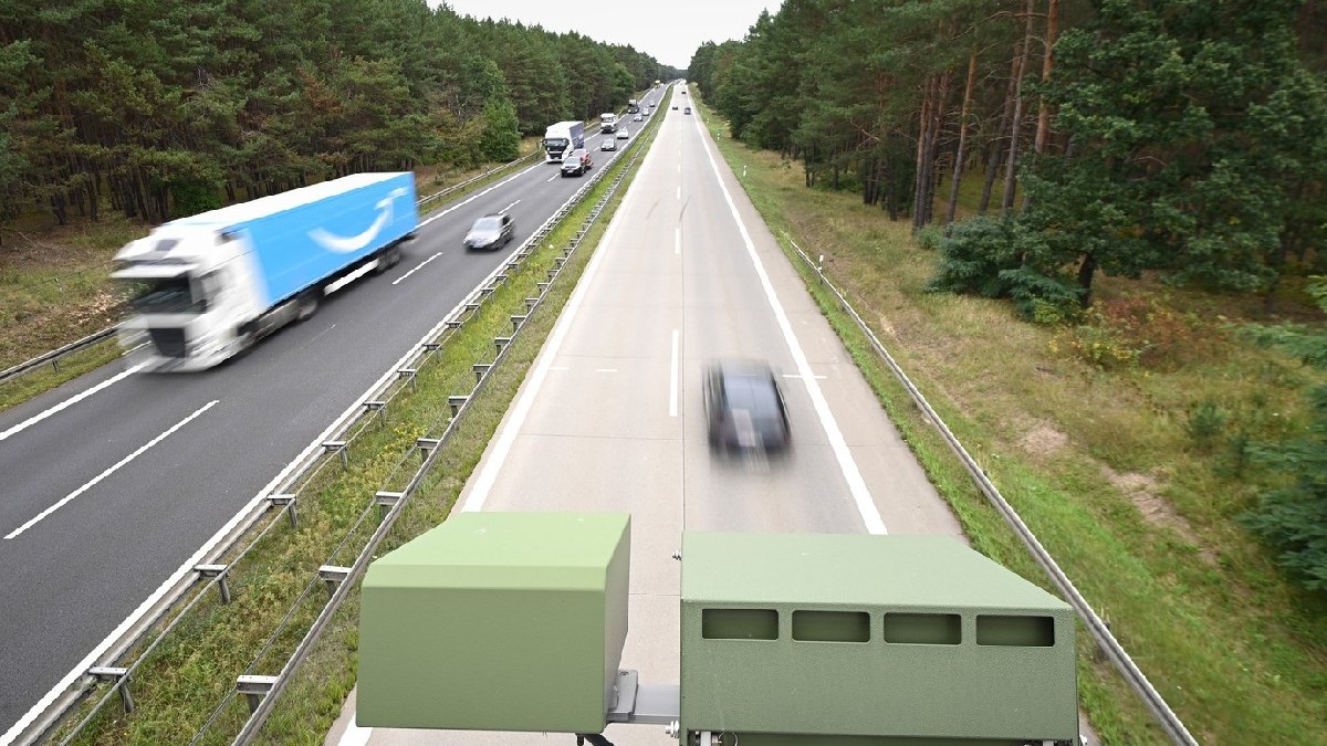 Un dispozitiv de recunoaștere a plăcuțelor de înmatriculare (KESY) este montat sub balustrada unui mic pod peste o autostrada în Germania