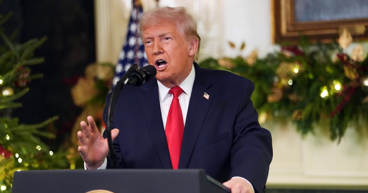 Președintele Donald Trump se adresează națiunii de la Casa Albă. Trump vorbeste de la tribuna, poarta un costum albastru închis, camasa alba si cravată roșie și gesticulează cu mâna