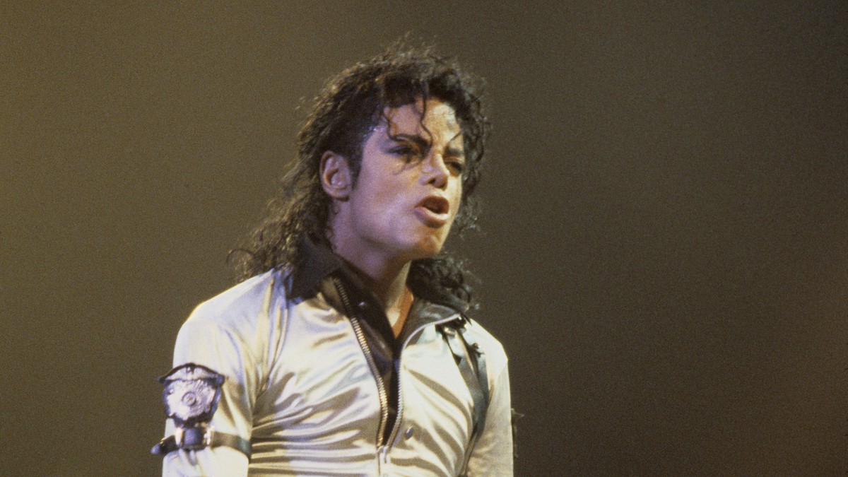 Michael Jackson în timpul unui concert, îmbrăcat într-o bluză aurie, cu guler maro și detalii de piele pe braț