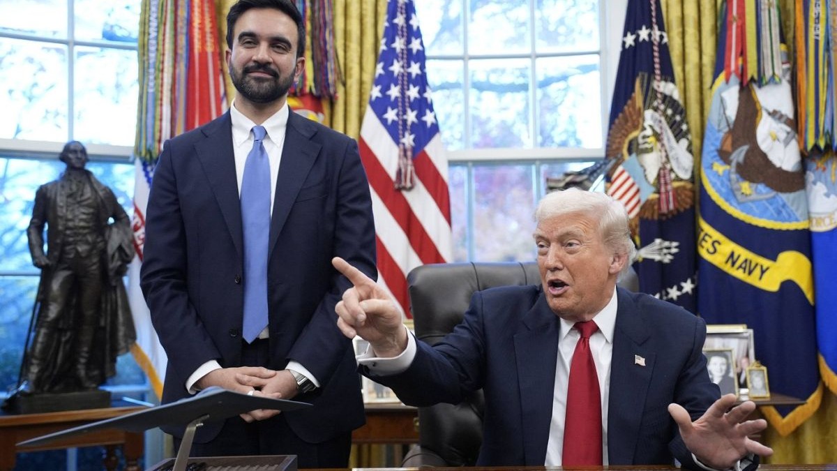 Donald Trump vorbește arătând cu mâna în timp ce stă la biroul de la Casa Albă, iar Zohran Mamdani în ascultă zâmbind, stând în picioare, 21 noiembrie 2025