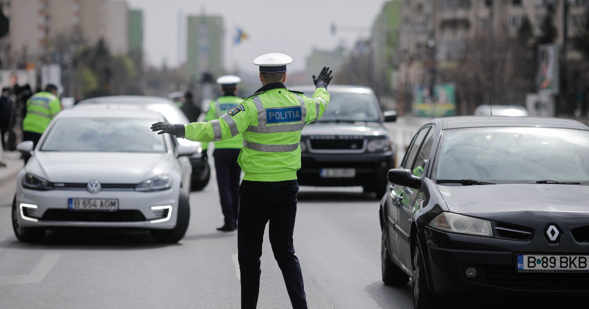 În imagine se vede un polițist rutier care dirijează traficul pe un bulevard urban, oprind mai multe autoturisme pentru control. Mașinile sunt aliniate pe carosabil, iar prezența agenților sugerează o acțiune de verificare sau un filtru rutier.
