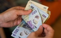 Imaginea prezintă mâinile unei persoane care numără un teanc de bancnote românești de 100 de lei.