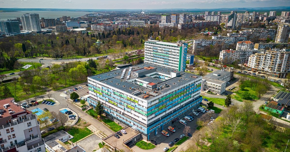 Spitalul municipal din orașul Burgas, Bulgaria, văzut de sus cu drona. În parcare se văd câteva mașini de ambulanță, copaci și alte clădiri în jur, iar în spate este marea.