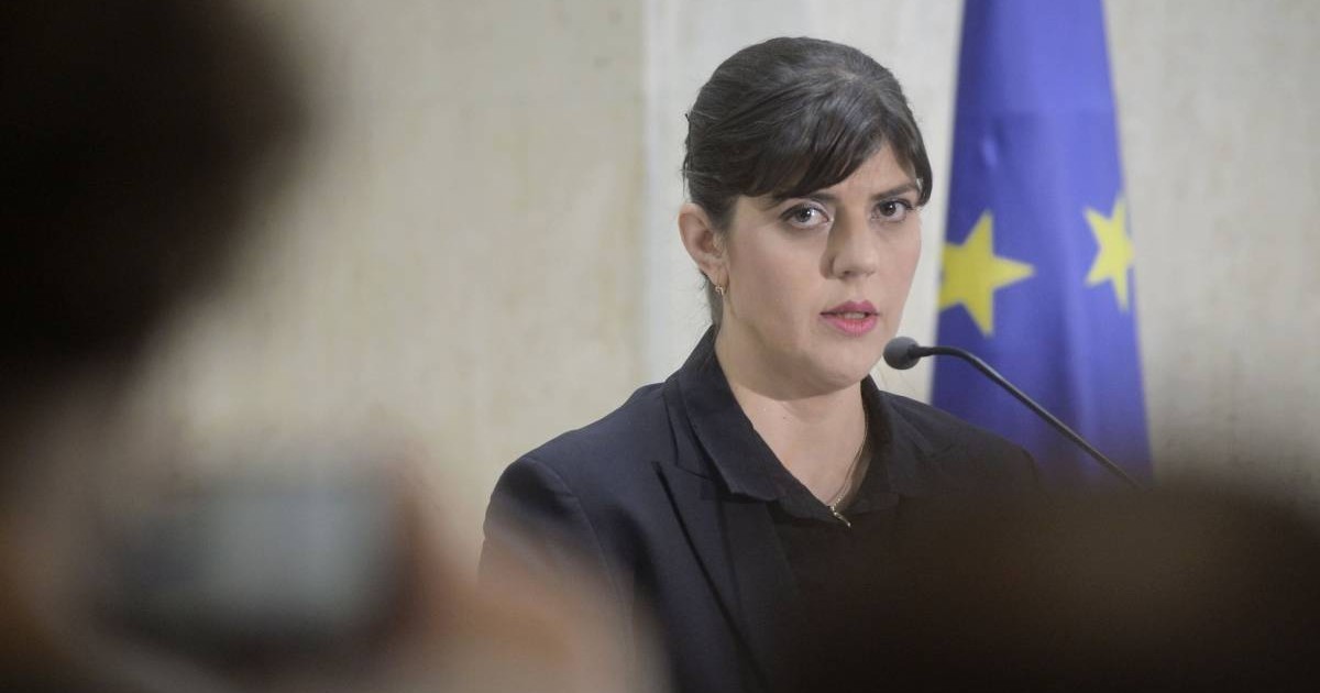 Laura Kodruta Kovesi, în timpul unei conferințe de presă în 2018, poartă un costum negru din două piese și vorbește la microfon în timp ce un jurnalist o fotografiază