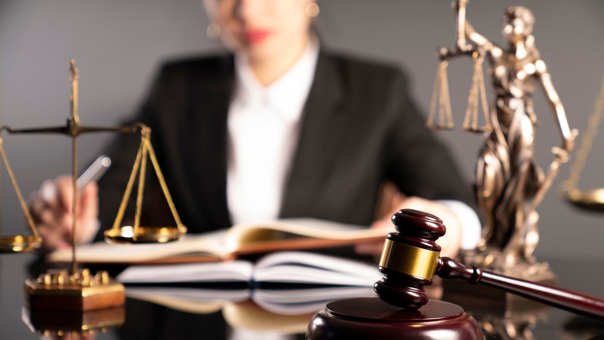 Ce face un notar – lista notarilor din București - Imagine cu mai multe obiecte de pe biroul unui notar, o balanţă, o statuie a zeiţei Themis şi un ciocănel de justiţie, aflate pe un birou, în faţa unei femei