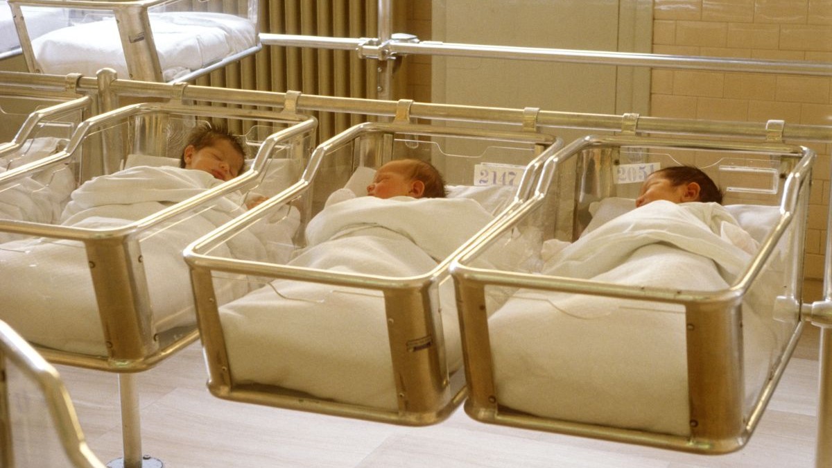 Trei nou-născuți stau fiecare în pătuțul lor, într-o secție a unui spital