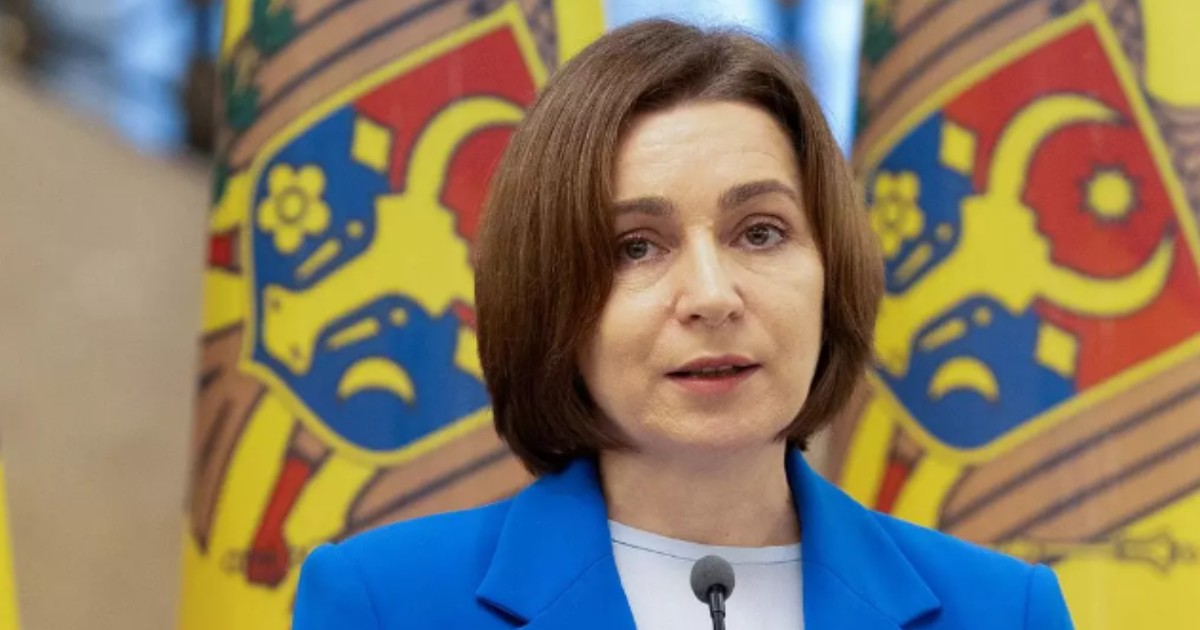 În imagine este ilustrată Maia Sandu, în sacou albastru, în timp ce vorbește la microfon