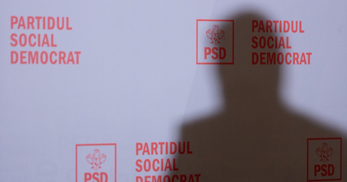 Silueta unui bărbat în dreptul unui panou pe care sunt trecută sigla și logo-ul Partidului Social Democrat