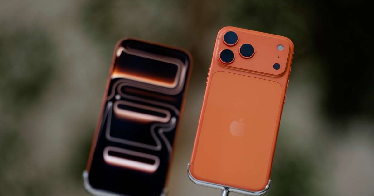 Două iPhone-uri 17 Pro, de culoare portocalie, unul cu fața, celălalt cu spatele, pe standuri de prezentare.