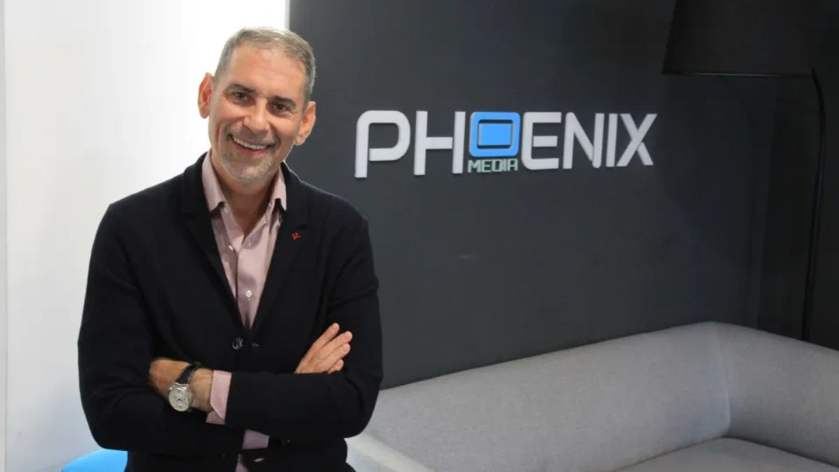 Dio Boacă, îmbrăcat cu un sacou negru și cămașă, iar pe fundal un perete cu logo-ul Phoenix Media