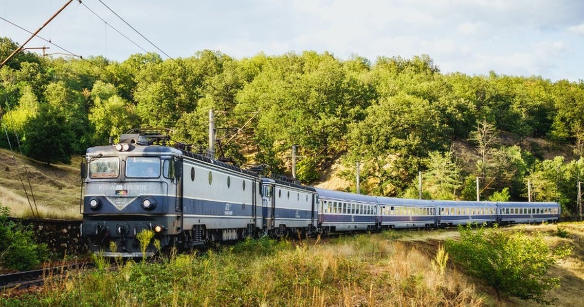Un tren CFR albastru format din mai multe vagoane merge pe șine într-o zonă verde