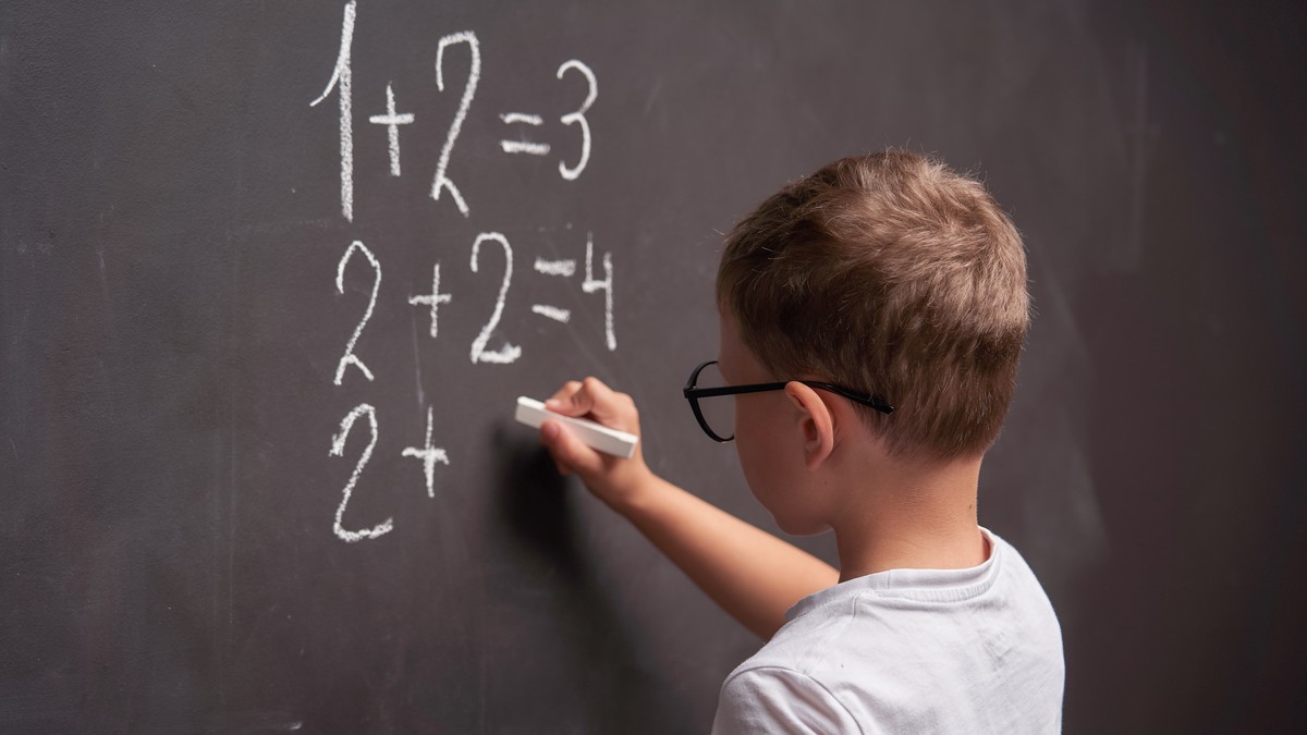 Elev de vârstă mică face calcule la matematică cu creta pe o tablă la școală.