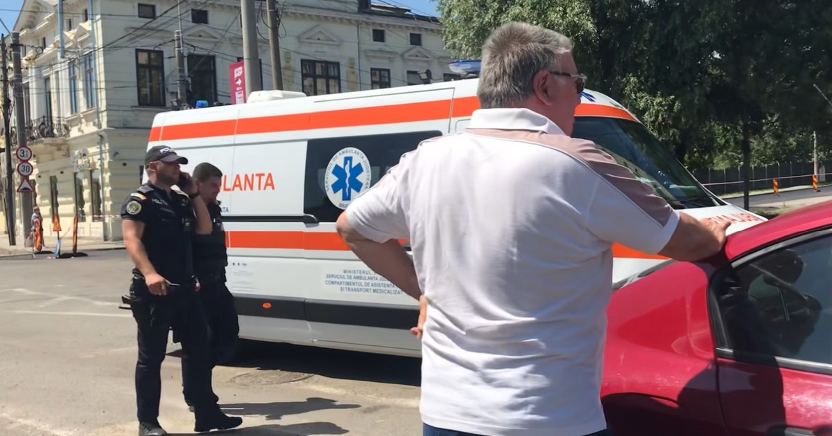 Doi polițiști trec pe lângă o ambulanță, în timp ce un bărbat în cămașă albă dă declarații după ce un tânăr a fost înjunghiat pe o stradă din Brăila, iulie 2025