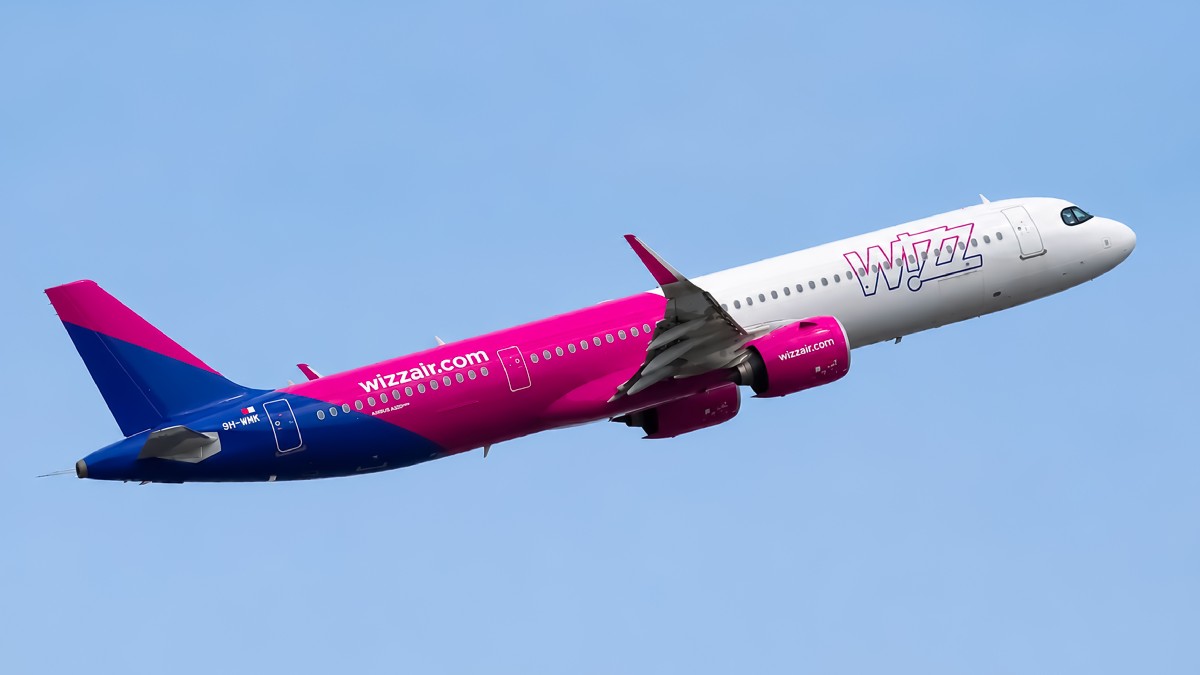 Imaginea surprinde un avion Wizz Air în plin zbor, sub un cer senin.