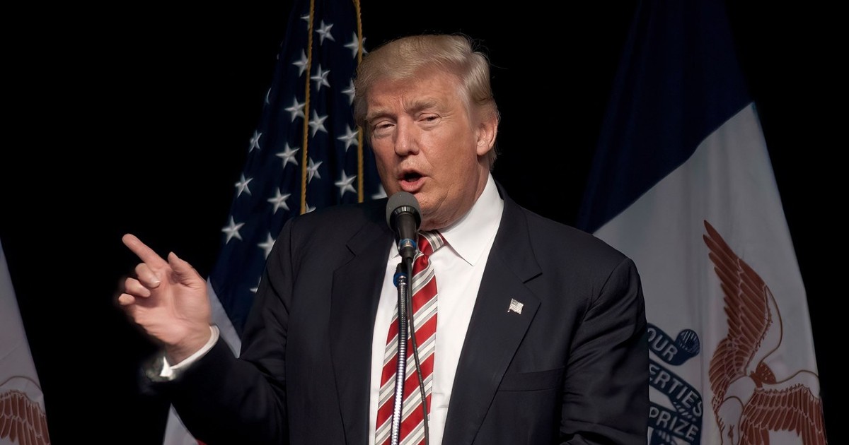 Donald Trump cu steagul SUA în spate și arătând cu degetul