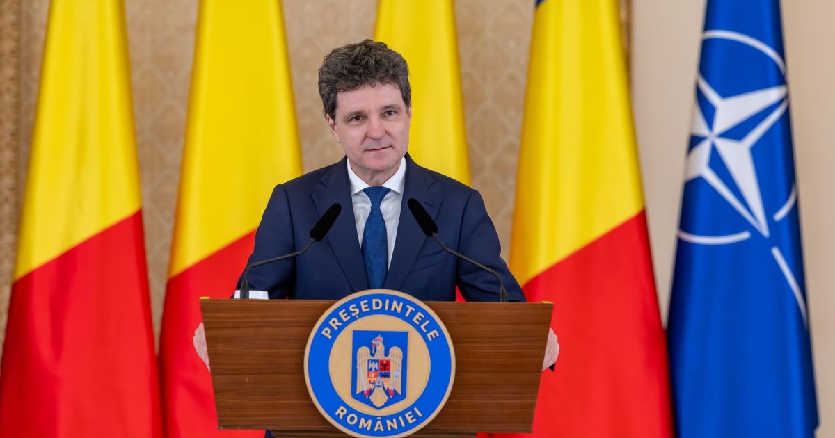 Nicușor Dan, îmbrăcat în costum albastru, cămașă albă și cravată albastră, la pupitrul de la Palatul Cotroceni, cu steagurile României și NATO pe fundal