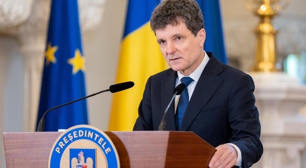 Imaginea îl prezintă pe Nicușor Dan vorbind de la o tribună oficială, având în fundal steagurile României și Uniunii Europene.