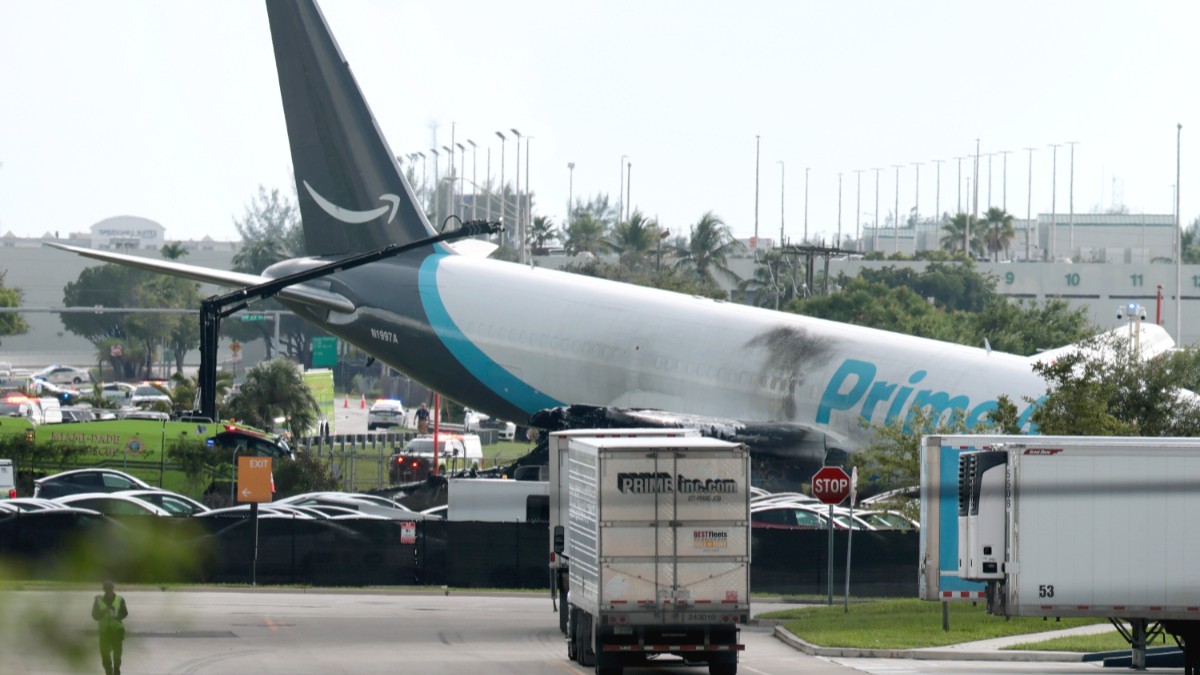 Imaginea prezintă un avion de marfă Prime Air avariat, oprit pe iarbă în apropierea unei zone de parcare, cu urme vizibile de arsuri pe fuzelaj.