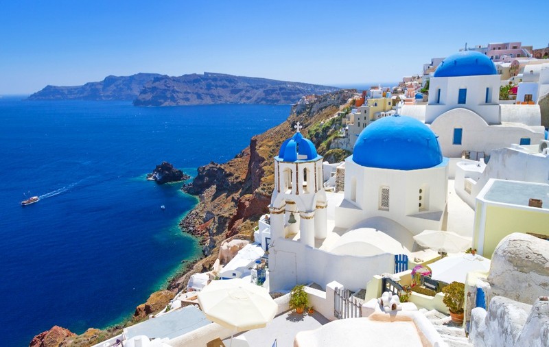 Peisaj din Santorini, clădiri albe construite pe stânci, privind spre apele albastre ale Mării Egee.