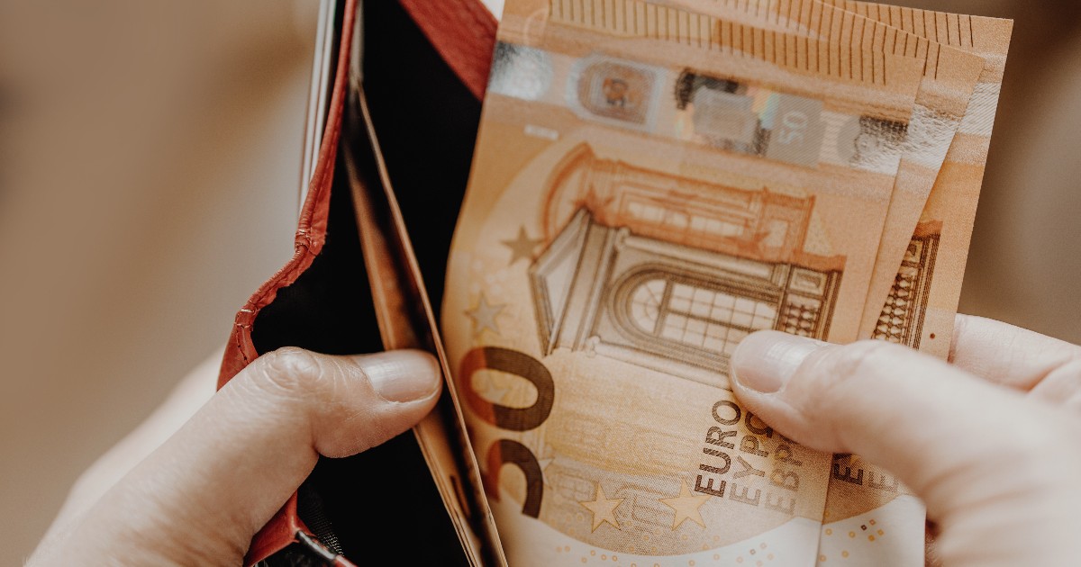 O persoană ține în mână câteva bancnote de euro, scoase dintr-un portofel aproape gol. Imaginea sugerează preocupări financiare și gestionarea atentă a banilor în context economic incert.