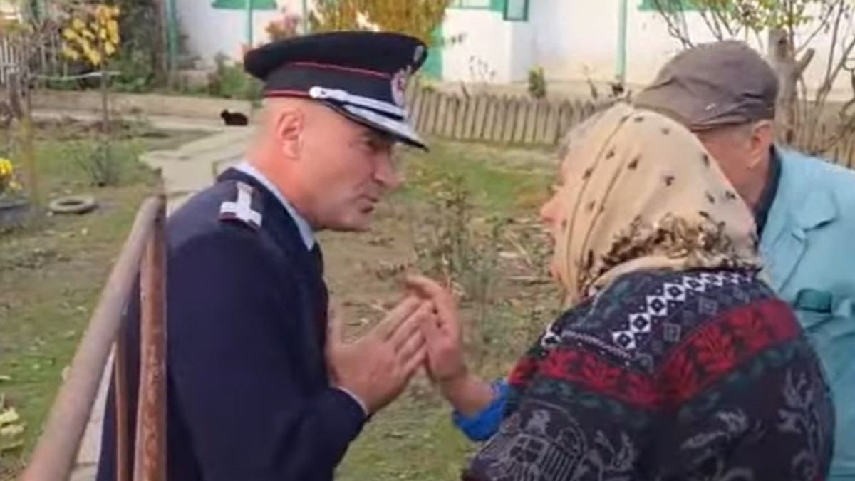 o femeie cu batic crem, îmbrcată într-un pulover tricotat multicolor, vorbește fața în fața cu șeful ISU Tulcea, îmbrăcat în uniformă, stând cu mâinile împreunate în fața femeii în semn de rugăminte