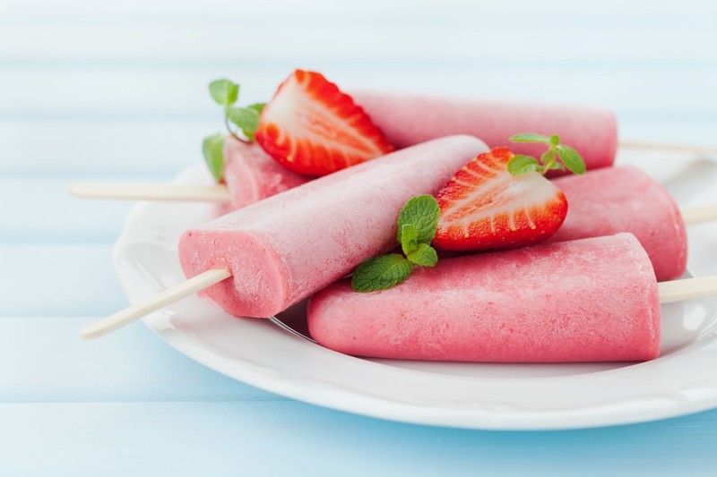 55849053 - homemade strawberry ice cream or popsicles in plate on blue wooden table, frozen fruit juice, selective focus