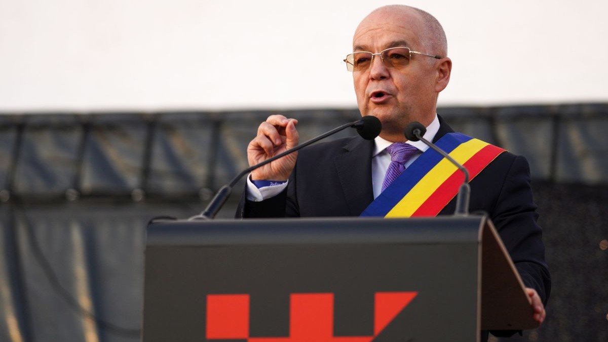 Emil Boc vorbește de la tribună la un eveniment din Cluj, în costum și având o eșarfă tricoloră, iunie 2025
