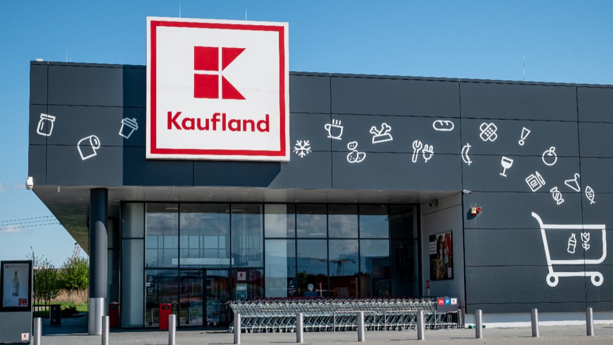 Fațada unui magazin Kaufland, cu sigla mare pe fundal gri decorat cu pictograme albe, având la intrare rânduri de cărucioare pentru cumpărături.