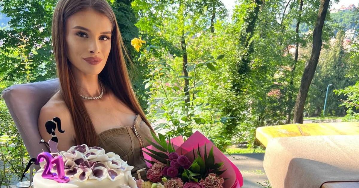 Teodora Marcu de la Insula iubirii îmbrăcată într-o rochie maro, pe o terasa la un restaurant cu un tort în mână, în ziua în care a împlinit 21 de ani.