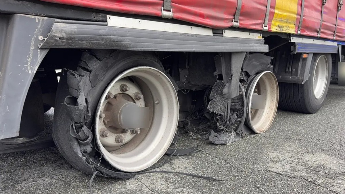 Partea inferioară a unei remorci de camion ale cărei anvelope sunt sever deteriorate și sfâșiate, lăsând jantele expuse direct pe carosabil.