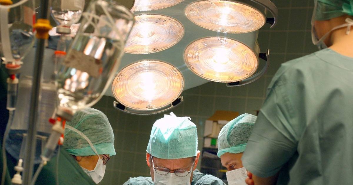 În imagine câțiva chirurgi se află în sala de operație, sub lumină puternică