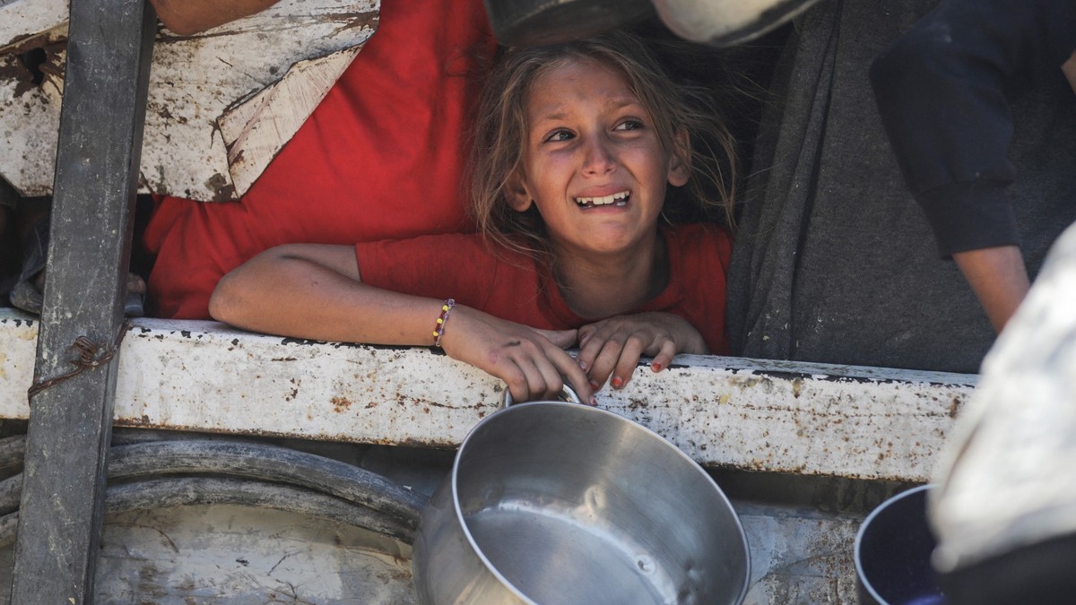 Imagine cu o fetiță care ține într-o mână o oală goală, în Gaza. Foto din 25 iulie 2025. Poartă o bluză roșie