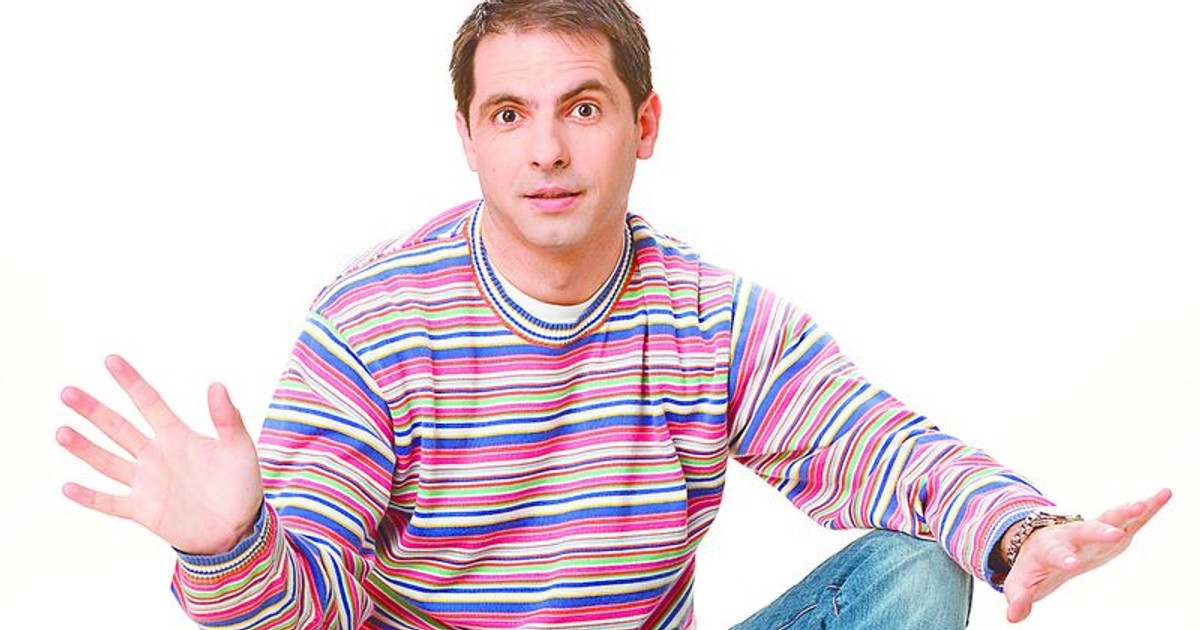 dan negru, îmbrăcat în blugi și un tricou colorat, stă așezat pe podea și gesticulează