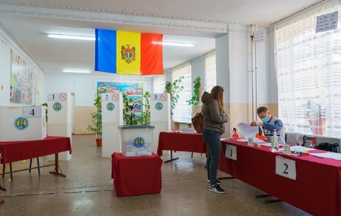 O femeie se află într-o secție de vot în Republica Moldova și așteaptă să fie găsită pe listele electorale de un funcționar, pentru a verifica prezența ei pe lista alegătorilor, înainte de a-i înmâna buletinul de vot